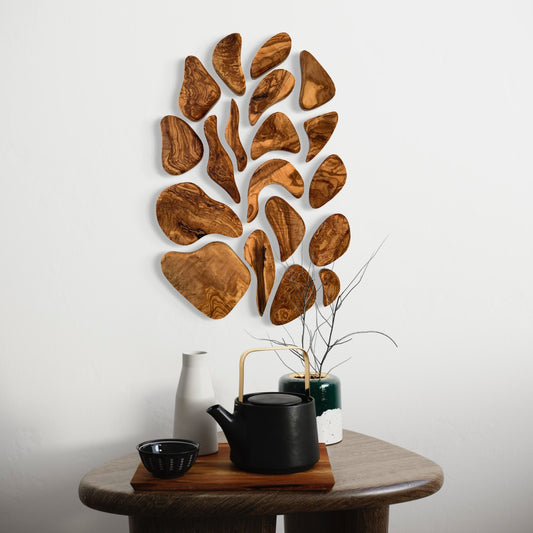 Wooden wall art piece on a white wall with a wooden table and tea set in the foreground.